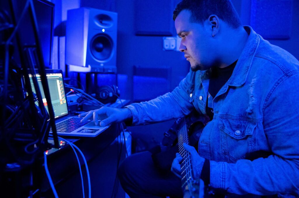 Guitarist recording his guitar using a laptop, electric guitar, DAW and virtual amp software.